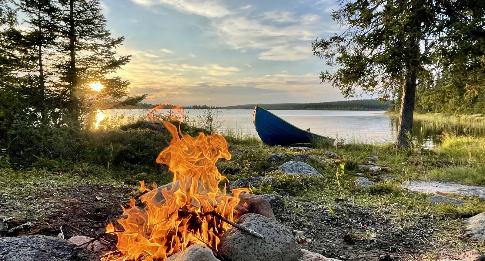Guests campfire by the lake and forests near ÁILU Hotel in Lannavaara, with views toward the Arctic wilderness of Swedish Lapland