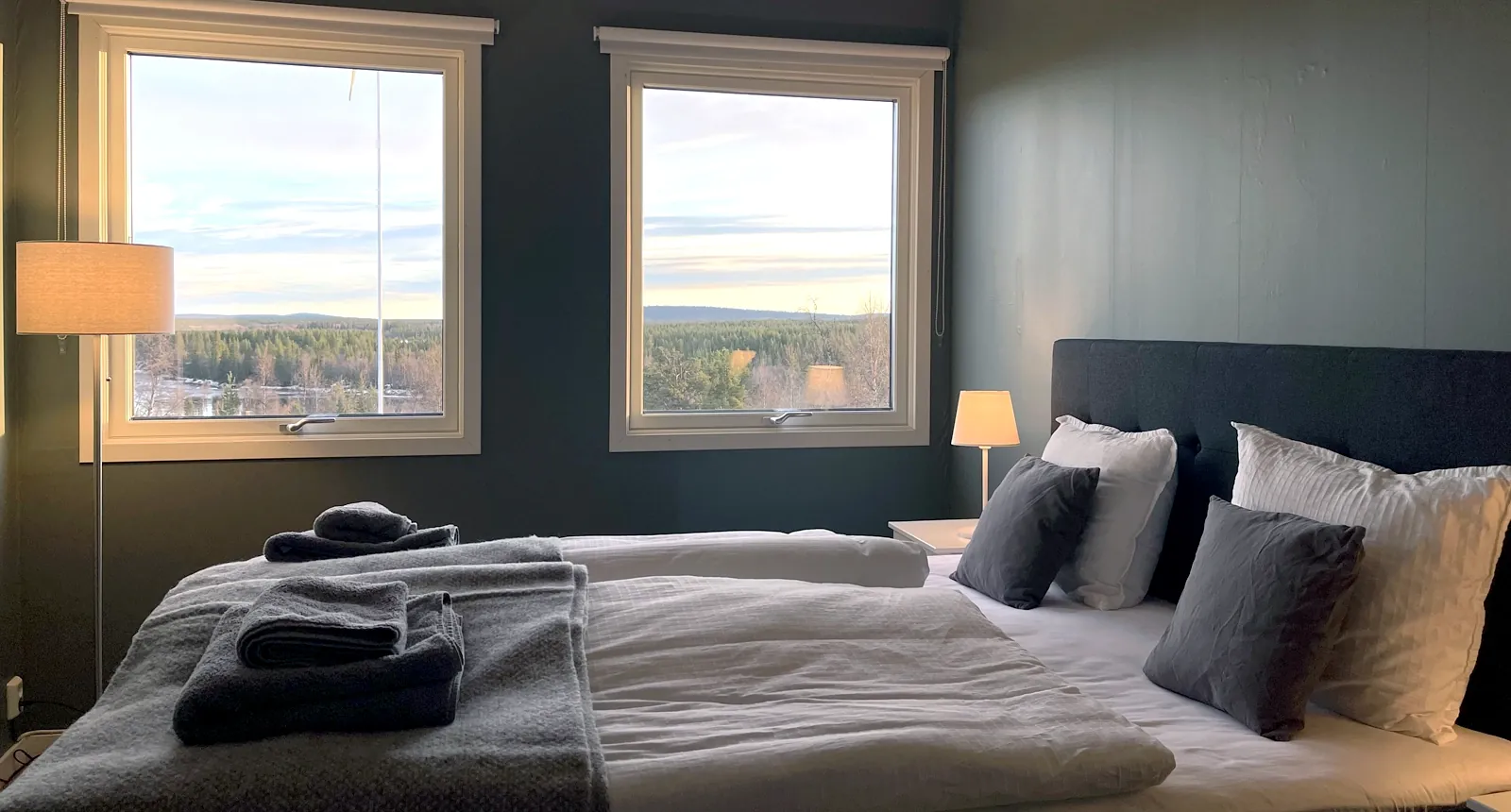 Interior view of ÁILU Hotel's Scandinavian-style room with double bed, natural light, and forest views in Swedish Lapland